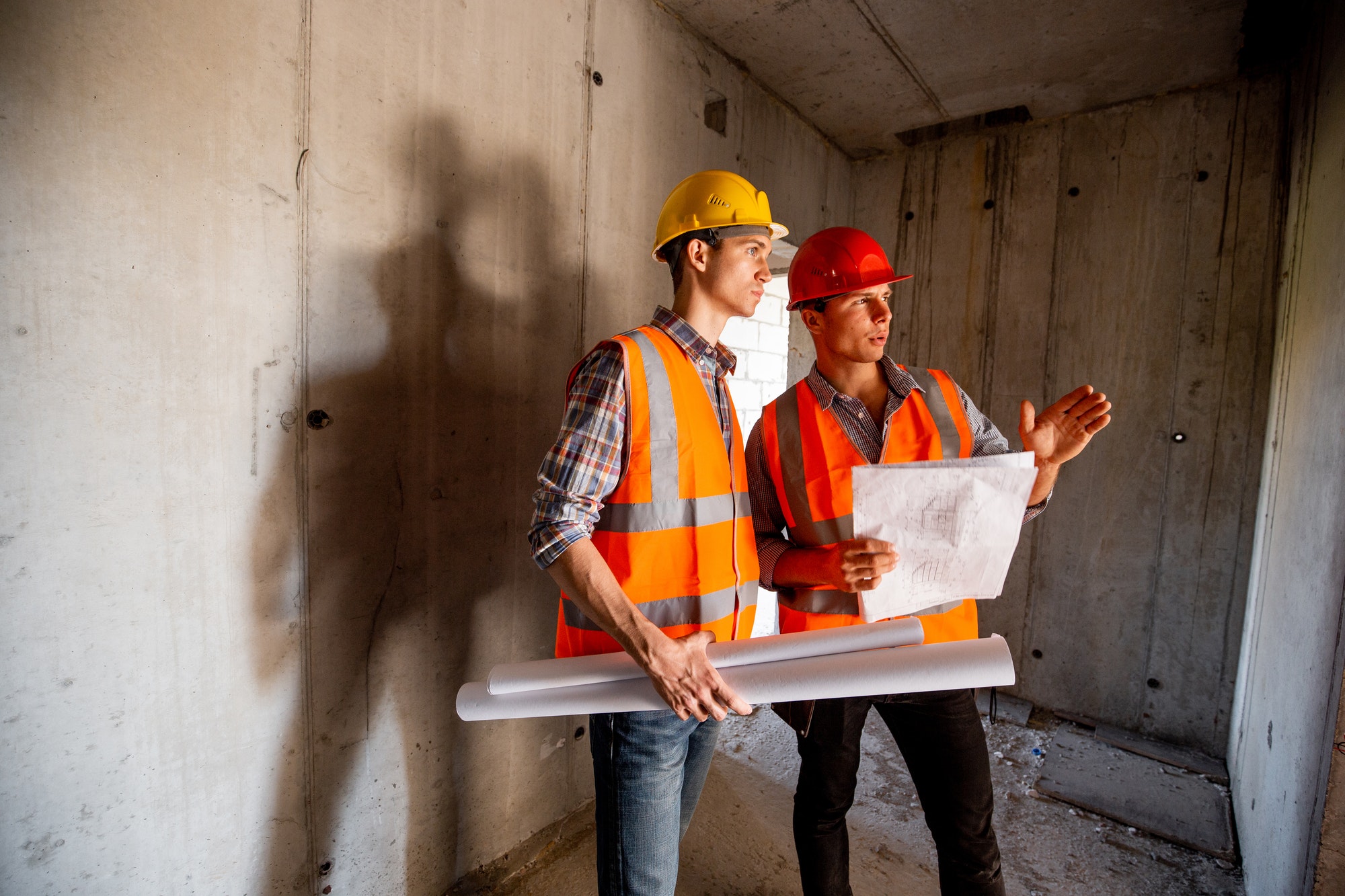 Construction manager and engineer dressed in orange work vests and helmets work with construction