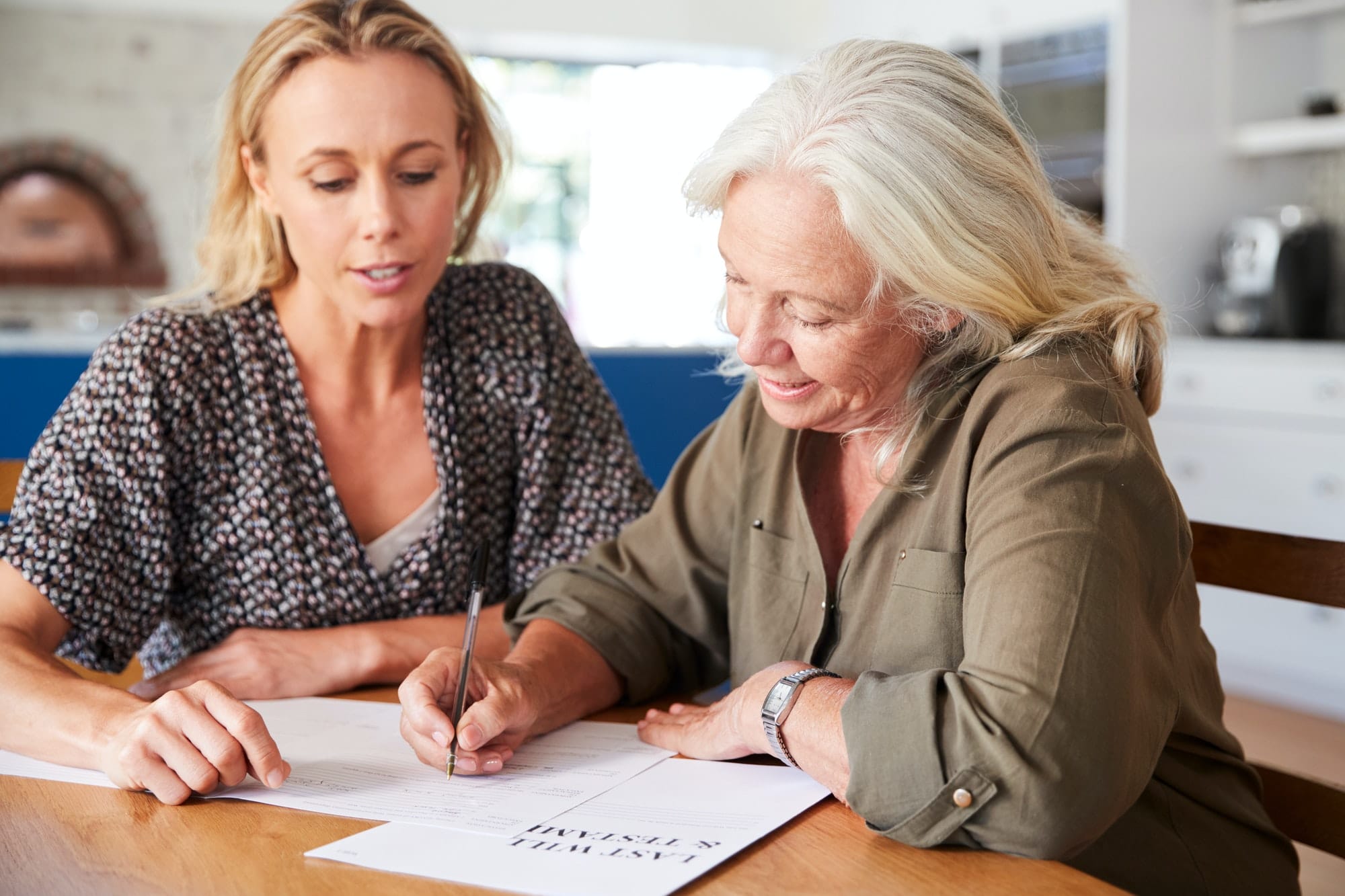 Female Friend Helping Senior Woman To Complete Last Will And Testament At Home